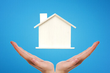 Hands holding a wooden house between their palms on blue background