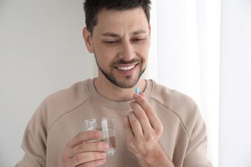 Man with glass of water taking pill at home - obrazy, fototapety, plakaty