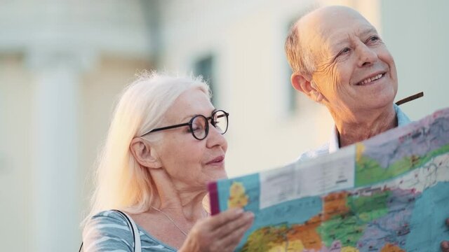 A cheerful elderly tourists couple man and woman are looking map while walking in the city