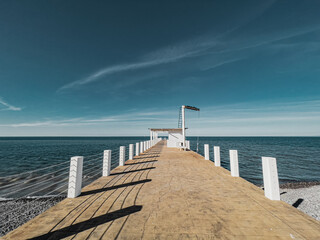Beautiful view at the black sea and blue sky from the wooden pier with posts and ropes. Calm serene tranquil aquamarine jetty landscape