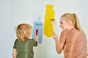 rear view on happy family mother and child son making repairs, paint the wall at home. view from...
