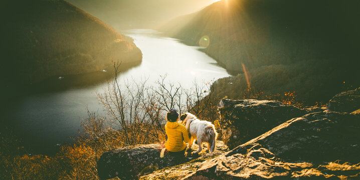 woman and her dog sitting on rock enjoying amazing autumn view over lake at sunset