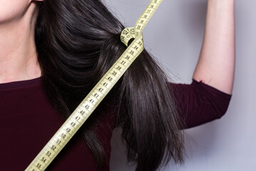 Detalle de una mujer sosteniendo una cinta métrica amarilla alrededor de un mechón de su cabello largo. Primer plano de una cinta de medir con números que se muestran. - obrazy, fototapety, plakaty