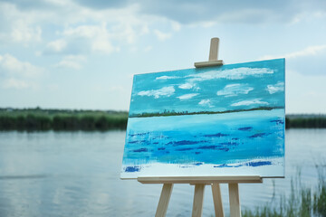 Wooden easel with unfinished painting near lake