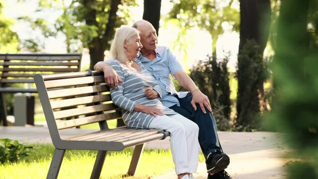 A happy elderly couple man and woman are sitting on the bench in the park