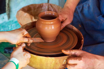 Potter makes on the pottery wheel clay pot and conducts a master class. Hands of the master and child close-up during work. Ancient national craft