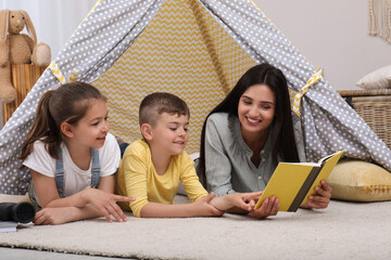Mother with children reading book in wigwam at home © New Africa
