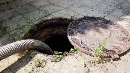 Open sewer manhole in the courtyard of a private house next to a fir tree. cleaning of the sewer