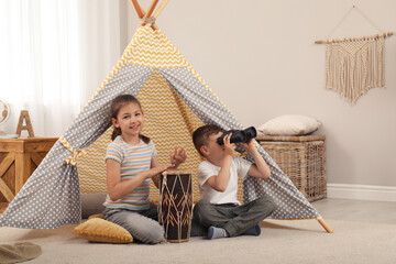 Cute little children playing in toy wigwam at home © New Africa