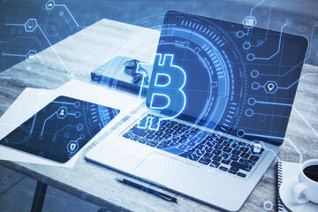 Creative glowing blue digital bitcoin hologram and laptop on office desktop background. Cryptocurrency and symbol concept. Landing page. Double exposure.