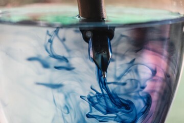 Close Up Image of Pen Dropped In a Glass of water and ink spread