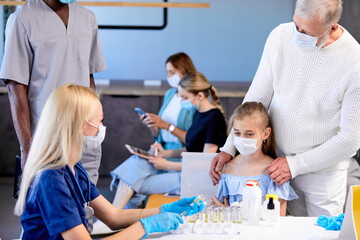 Fototapeta premium Mass immunization, scared child girl will get vaccination in hospital. Professional adult female nurse or doctor in gloves dials vaccine into syringe to inject to patient. focus on girl came with dad