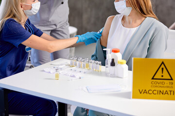 close-up Vaccine in the hand of young caucasian woman by female doctor.The concept of mass vaccination, against coronavirus. Genome, human modification. Problems, benefits and harms of vaccination