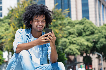 Latin american young adult man watching video clip with mobile phone outdoor in city