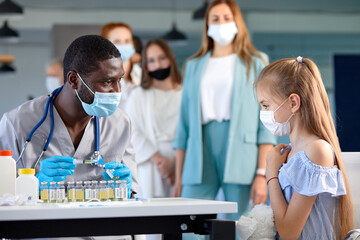 Black male doctor preparing to inject chilg girl patient with Covid 19 antiviral vaccine. Mass...