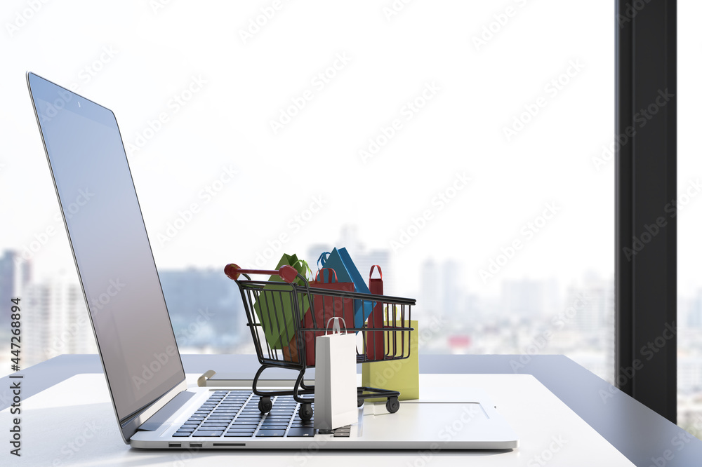 Poster close up of workspace with laptop and tiny shopping carts on keaybord. blurry window with city view 