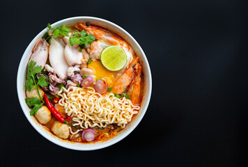 Hot and spicy noodle soup in white bowl on black background.