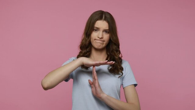 Need more time! Tired depressed wavy haired girl showing timeout gesture to camera and looking imploringly, asking for pause, declining suggestion.Indoor studio shot isolated over pink background.