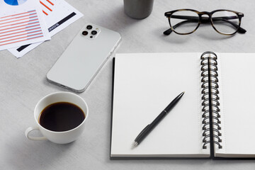 Blank notepad, coffee cup, mobile phone, glasses, financial report on the work table. 