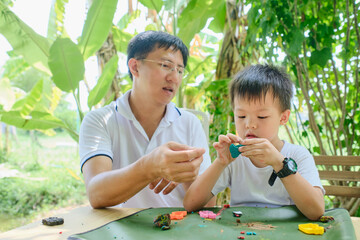 Parent sitting homeschooling with little kid, Asian Father and son having fun playing colorful modeling clay, Play dough at backyard garden on nature, Learning at Home, Fun home school concept