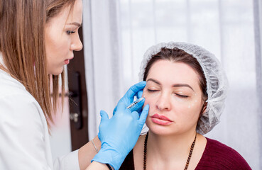 Injection facial rejuvenation. The beautician injects cosmetic injections into the facial muscles to smooth out wrinkles. Beautiful woman at the reception of the beautician.