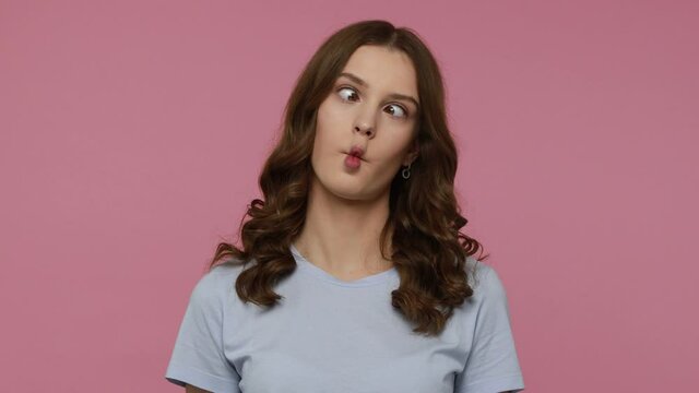 Humorous funny beautiful teenager girl in casual style T-shirt making fish face with pout lips and showing comical goofy grimace, childish behavior. Indoor studio shot isolated over pink background.