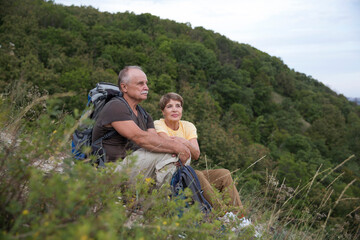 Naklejka na ściany i meble Senior tourist couple sitting on the mountain. Senior couple walking in nature. travel tourism concept. Outdoor activities on weekends.
