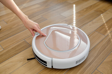 female push start button on robot vacuum cleaner. Modern smart household. Detail of hand that turns...