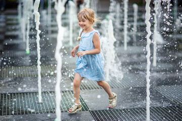 happy little girl running under splashing water