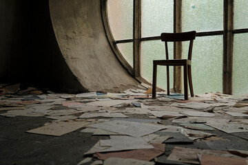Chair in front of a round window in an abandoned church with papers and book pages lying on the ground