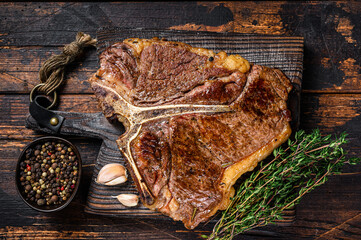 Roast t-bone or porterhouse beef meat Steak on a wooden cutting board. Dark wooden background. Top...