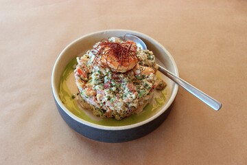 Rusk soaked in olive oil with shrimp, kopanisti cheese, tomatoes, peppers, caper, and aromatic herbs in a clay pot isolated on brown baking paper for the Greek meal of 