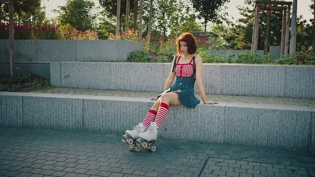 Gorgeous young woman in bright clothes wearing quads sitting on stairs in urban park outdoors, tracking shot