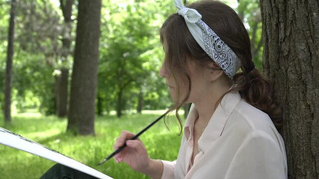 Young talented woman artist paints nature in a park or forest