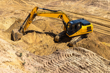 Closeup of an industrial yellow excavator working in a cave quarry. Industry, technology, mining. Heavy industrial machinery.