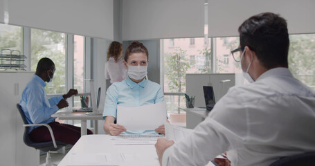 Female employer wearing face mask holding cv listening male candidate at job interview