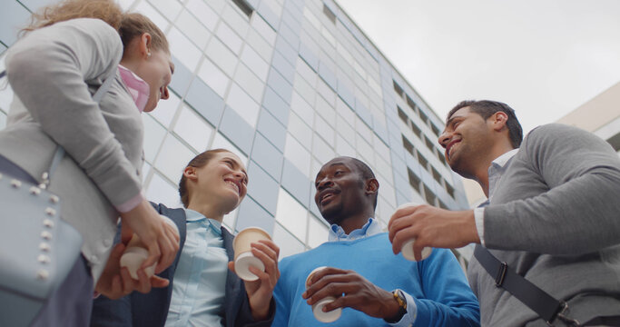 Bottom view of young colleagues outdoors drinking coffee, smiling and chatting