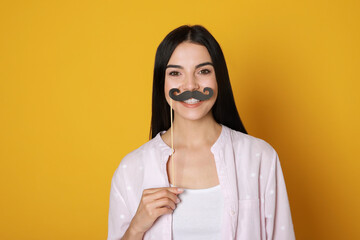 Pretty woman with fake mustache on yellow background