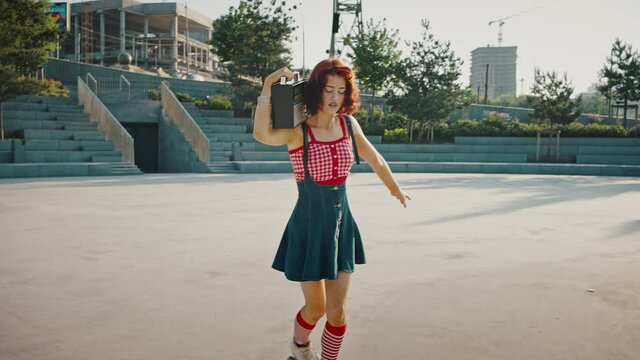 Young happy redhead lady roller skater skating on quads with vintage radio receiver on shoulder