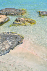 Sandy pink beach with rocky stones and azure sea water.
