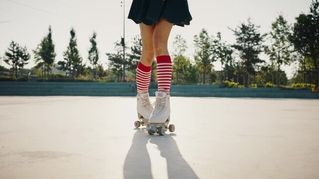 Close up of female legs in striped knee-highs rollerblading in urban park, young woman enjoying riding outdoors