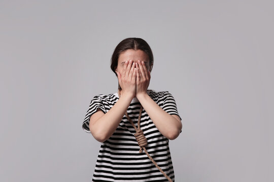 Depressed woman with rope noose on neck against light grey background