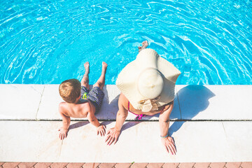 Young mother with son taking sun and sitting on the edge of the swimming pool