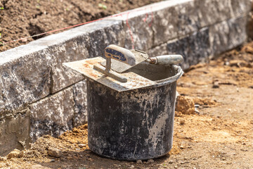 Brick trowels on a bucket at a building lot in front of a stonewall