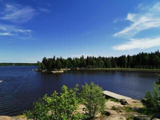 Naklejka premium View from the observation deck on the picturesque shore of the Vyborg Bay in the Monrepos Park of the city of Vyborg against the background of a blue sky with clouds.