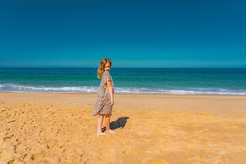 Young beautiful girl in beige dress staying along the sandy beach near the waves. High quality photo