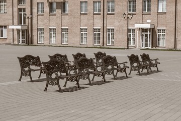 Group of empty vintage wooden benches with ornate black iron forged elements in small provincial town in sepia tone. Urban public vandal proof furniture.
