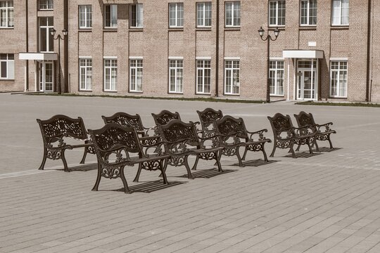Group of empty vintage wooden benches with ornate black iron forged elements in small provincial town in sepia tone. Urban public vandal proof furniture.