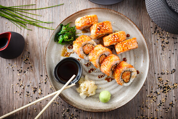 Baked sushi maki rolls with salmon, crab and spicy sauce on a plate with chopsticks, soy sauce, wasabi and ginger. Japanese traditional fish food closeup served for lunch in modern gourmet restaurant