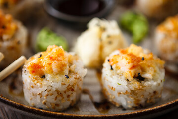 Baked sushi maki rolls with prawns and crab on a plate with chopsticks, soy sauce, wasabi and ginger. Japanese traditional fish food closeup served for lunch in modern gourmet restaurant